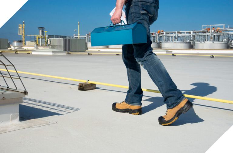 Worker with blue tool box walking across large flat building roof